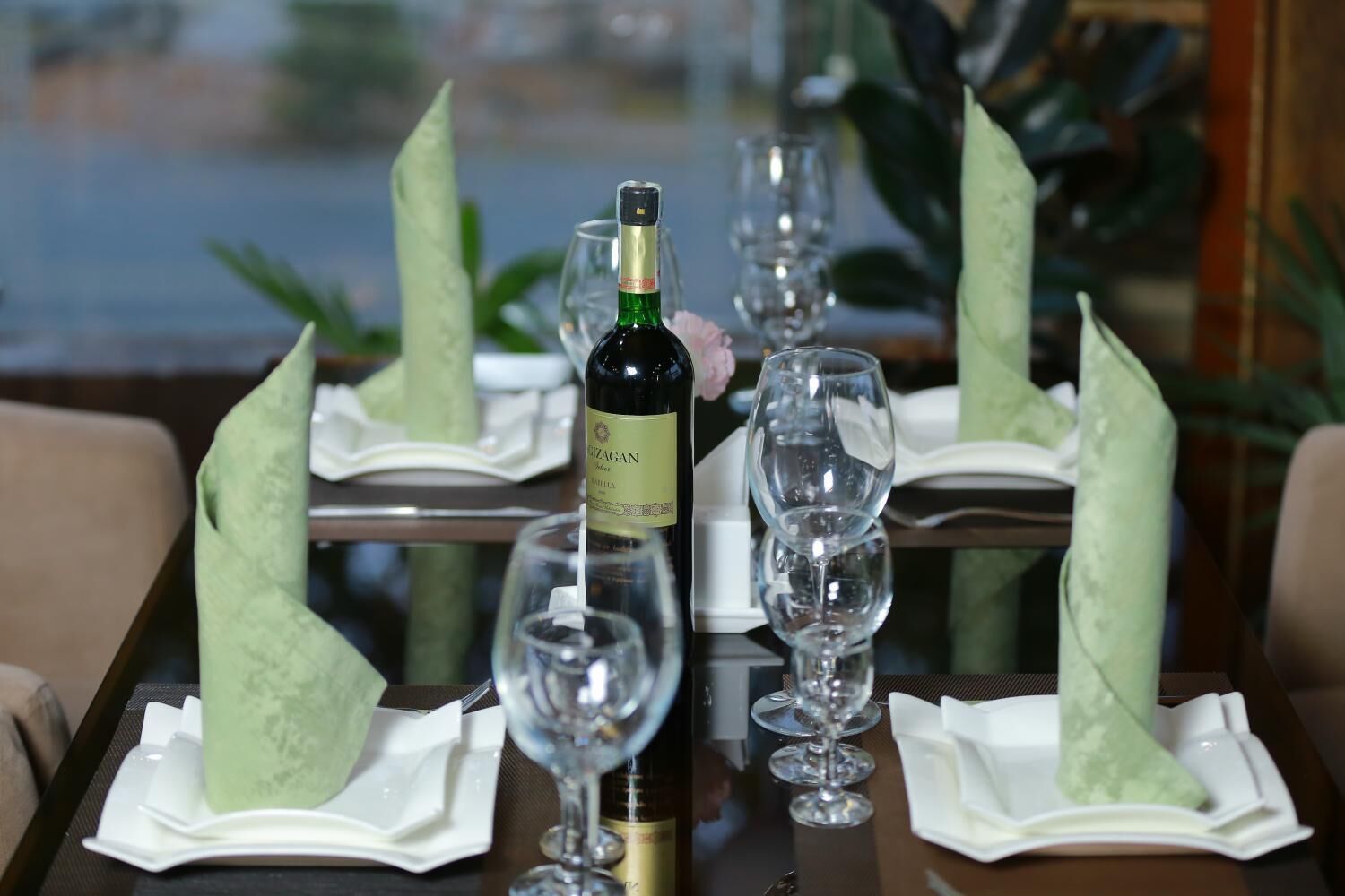 Une table mise pour un repas, avec une bouteille de vin, des verres propres et des serviettes pliées.