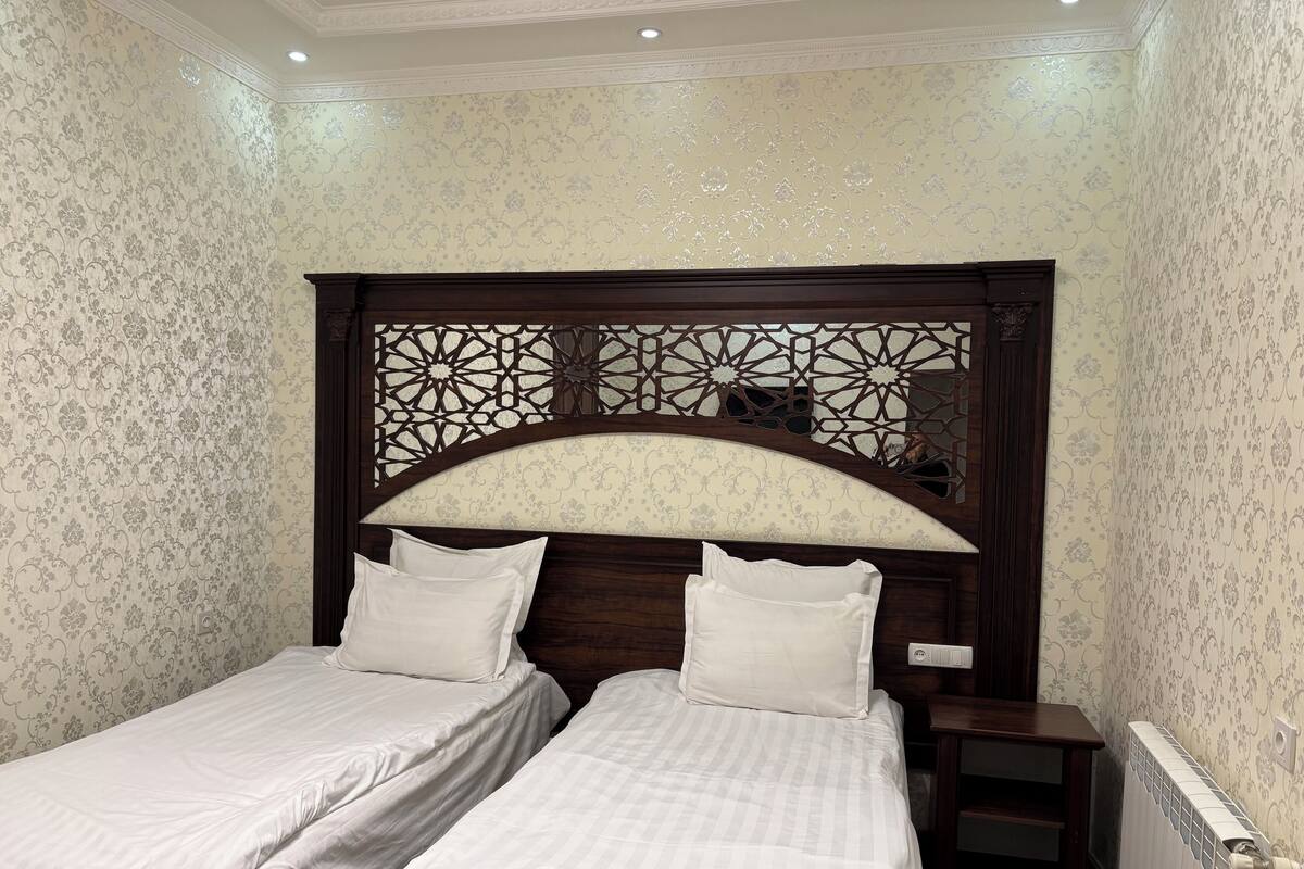 A bedroom with two single beds, a wooden headboard with intricate designs, and a radiator on the wall.