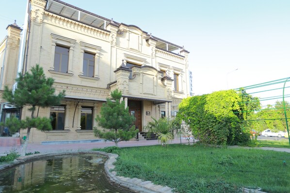A historic building with a large entrance, a small pond, and a well-maintained lawn.