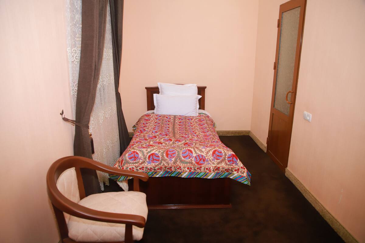 A small, neatly arranged bedroom with a single bed, a chair, and a door.
