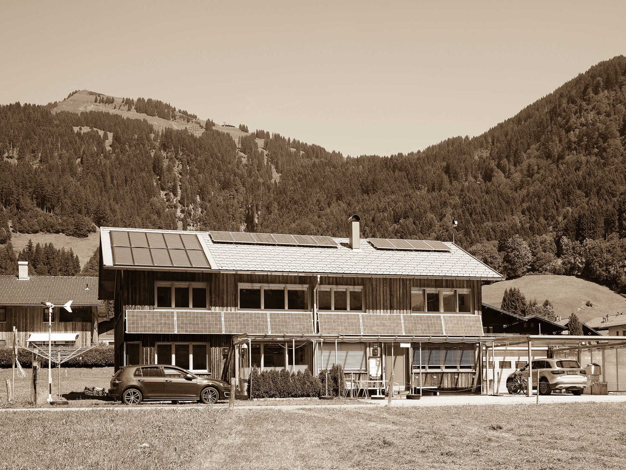 Ein zweistöckiges Gebäude mit einem geneigten Dach und Solaranlagen, vor der Tür ein Auto geparkt.