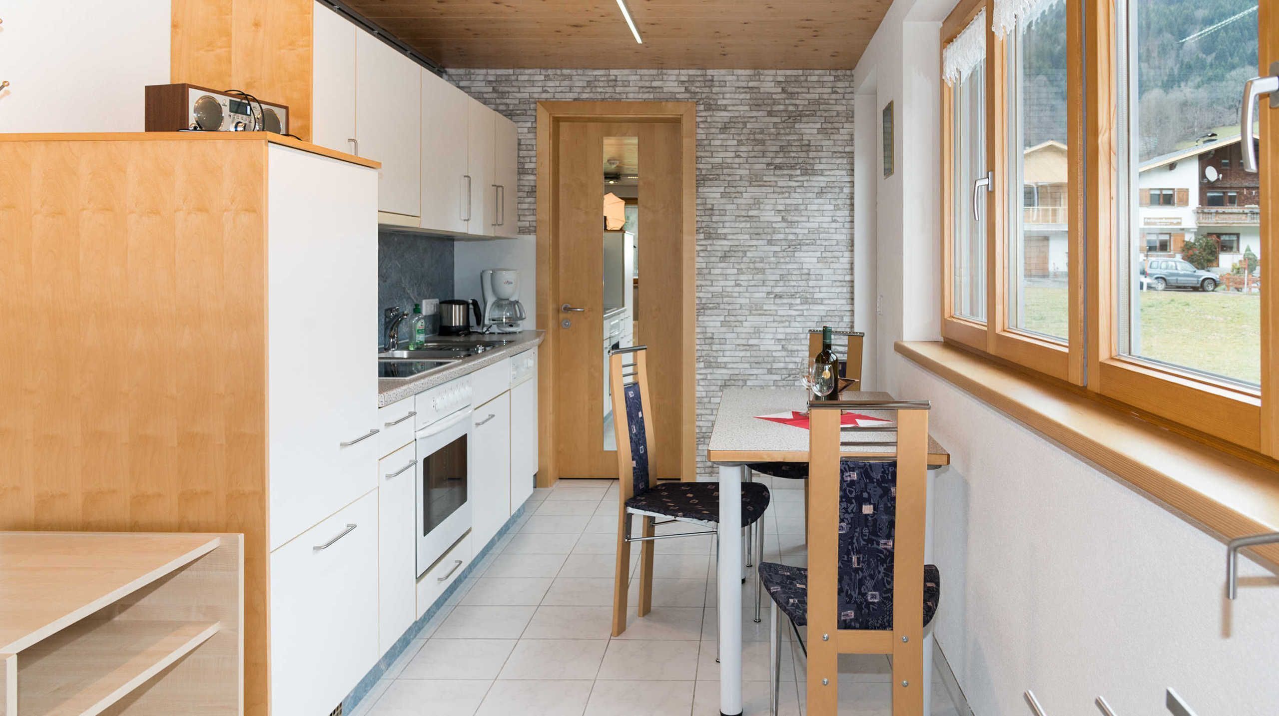 Cocina compacta con armarios blancos, encimera de madera y zona de comedor con mesa y sillas.