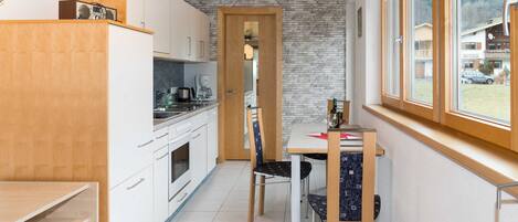 Cocina compacta con armarios blancos, encimera de madera y zona de comedor con mesa y sillas.