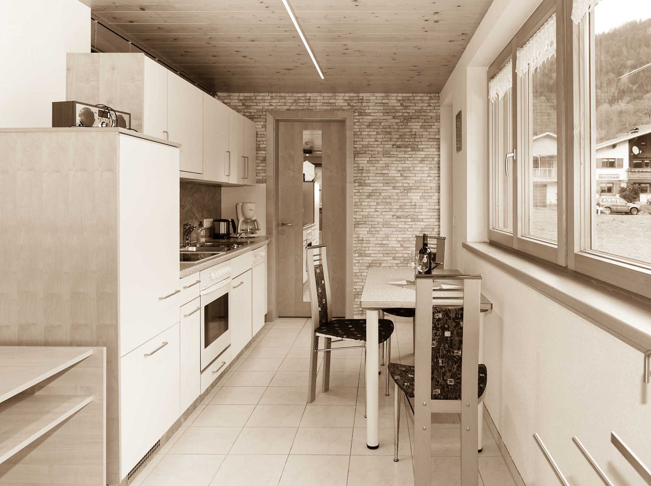 A compact kitchen with white cabinetry, a dining table with chairs, and a brick wall.