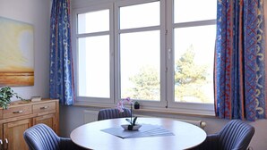 Une pièce avec une table ronde, quatre chaises, un radiateur et une fenêtre avec des rideaux.