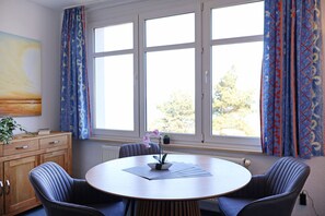 A room with a round table, four chairs, a radiator, and a window with curtains.