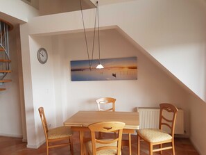 A dining area with a wooden table and chairs, a clock, a painting of a sunset, and a radiator.