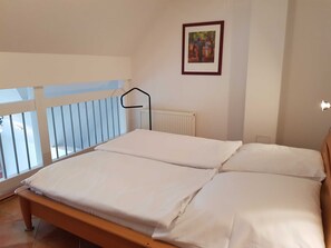A bedroom with a bed, a window with a view, a radiator, and a framed picture on the wall.