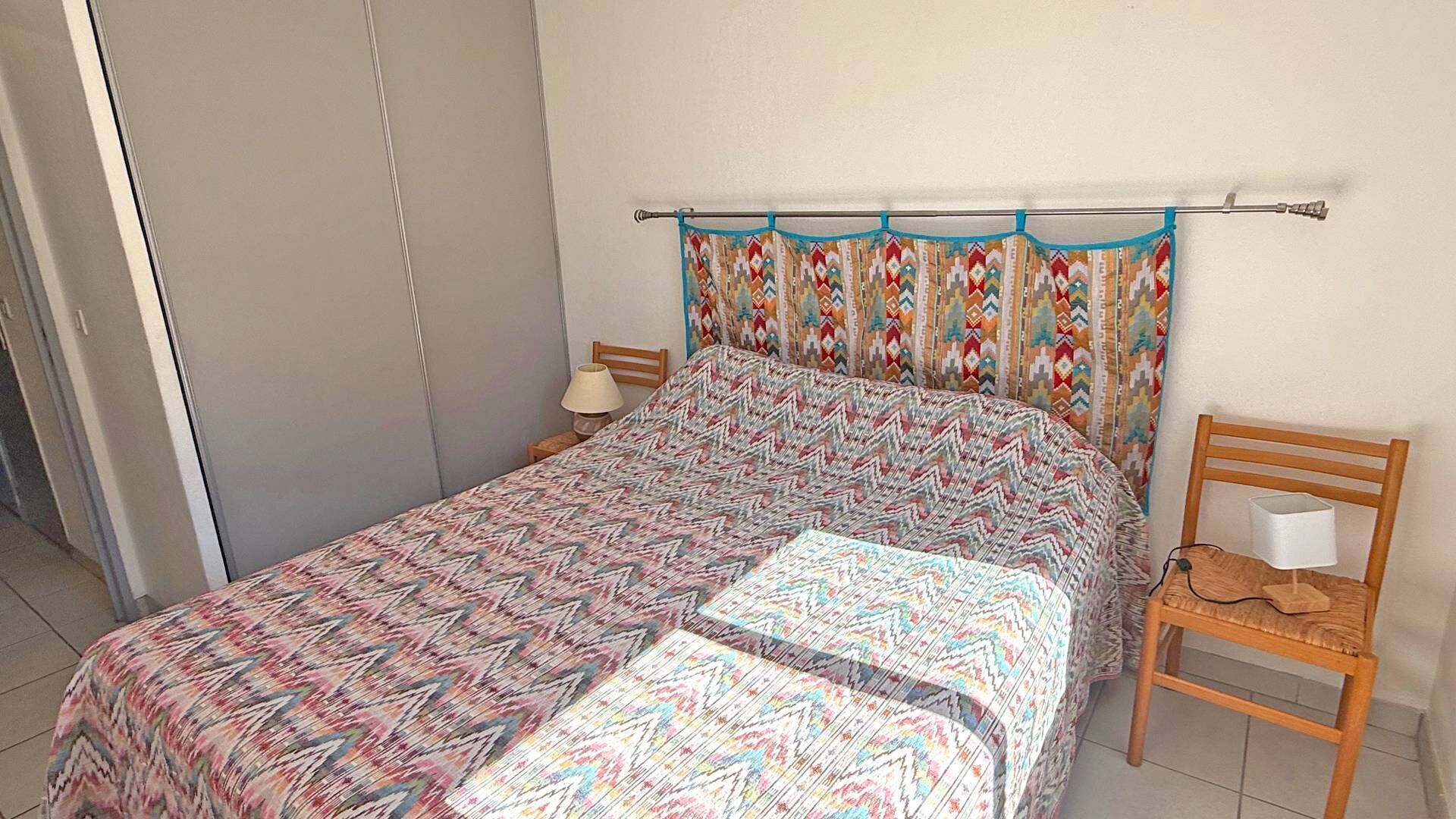 A bedroom with a bed, a nightstand, a chair, and a window with curtains.