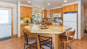 A kitchen with wooden cabinets, a granite countertop, and a central island with bar stools. - Heart of Truckee: Modern Truckee Escape with A/C, Kids' Room & Walkable Location (Truckee)