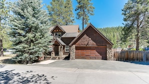 A log cabin with a stone foundation, a wooden garage, and a driveway leading to the entrance. - Heart of Truckee: Modern Truckee Escape with A/C, Kids' Room & Walkable Location (Truckee)