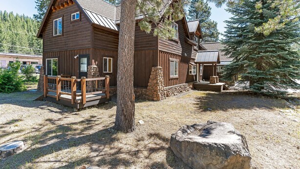 A rustic log cabin with a wooden deck, stone foundation, and a large rock in the foreground. - Heart of Truckee: Modern Truckee Escape with A/C, Kids' Room & Walkable Location (Truckee)