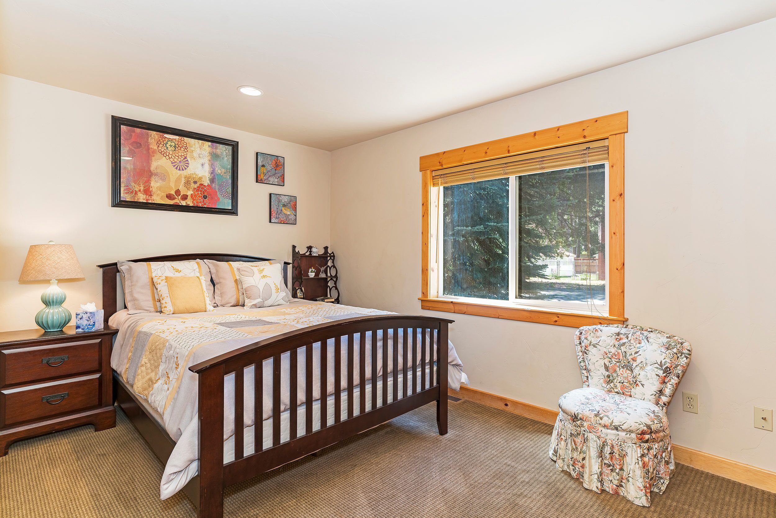 A bedroom with a wooden bed, a chair, a window, and artwork on the wall.