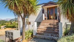A modern two-story house with a staircase leading to the front door, surrounded by palm trees and a gravel driveway. - Lake and Mountain Ridge - Queenstown Apartment (Queenstown)