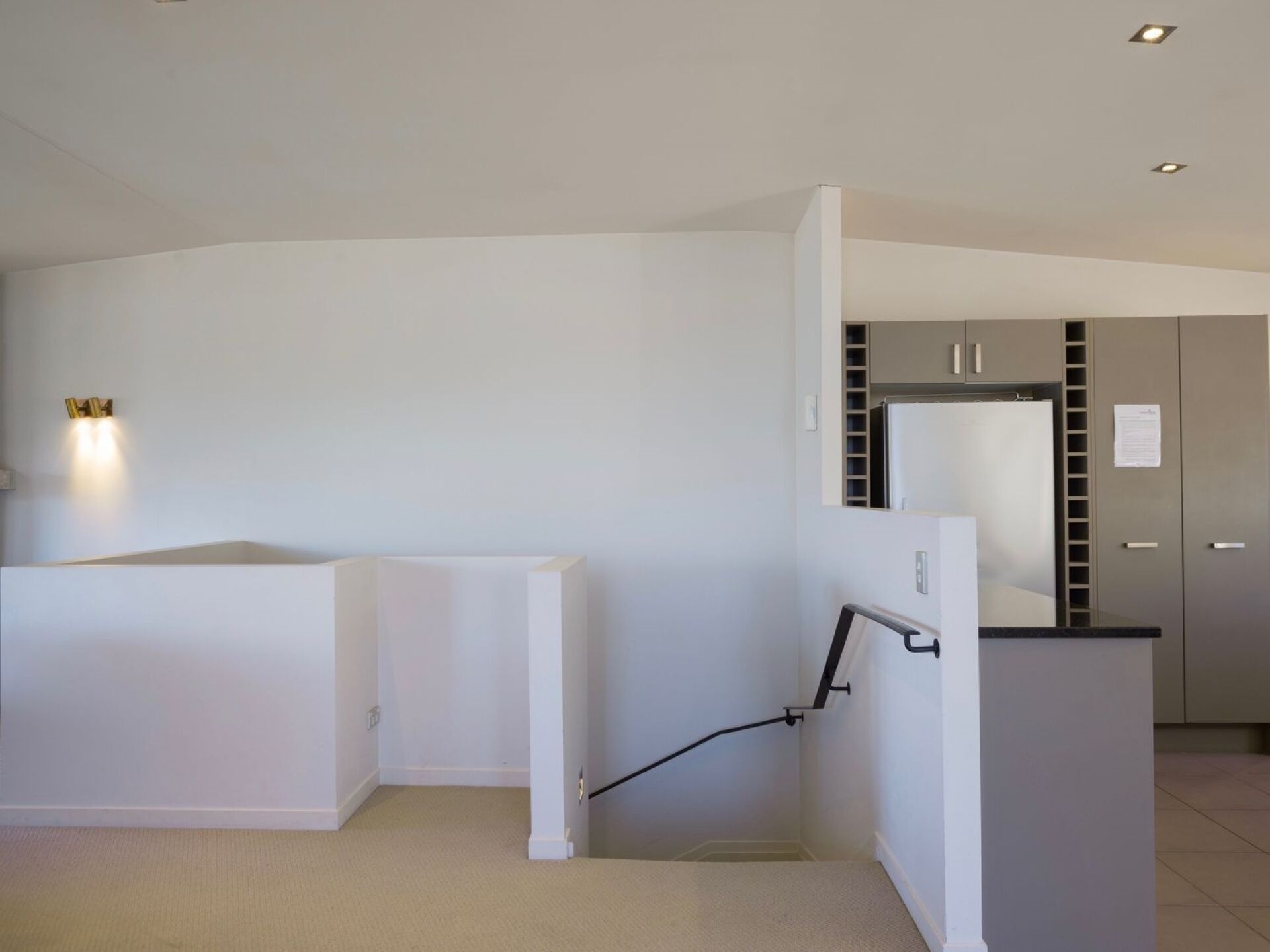 A modern, minimalistic room with a white wall, a built-in kitchen area, and a small seating area.
