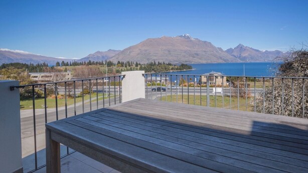 A wooden deck with a metal railing overlooking a lake and mountains. - Lake and Mountain Ridge - Queenstown Apartment (Queenstown)