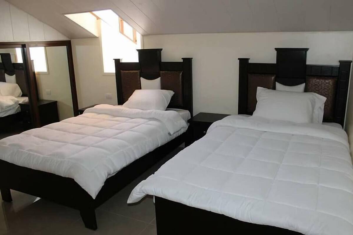 A hotel room with two beds, each with a wooden headboard and white bedding.
