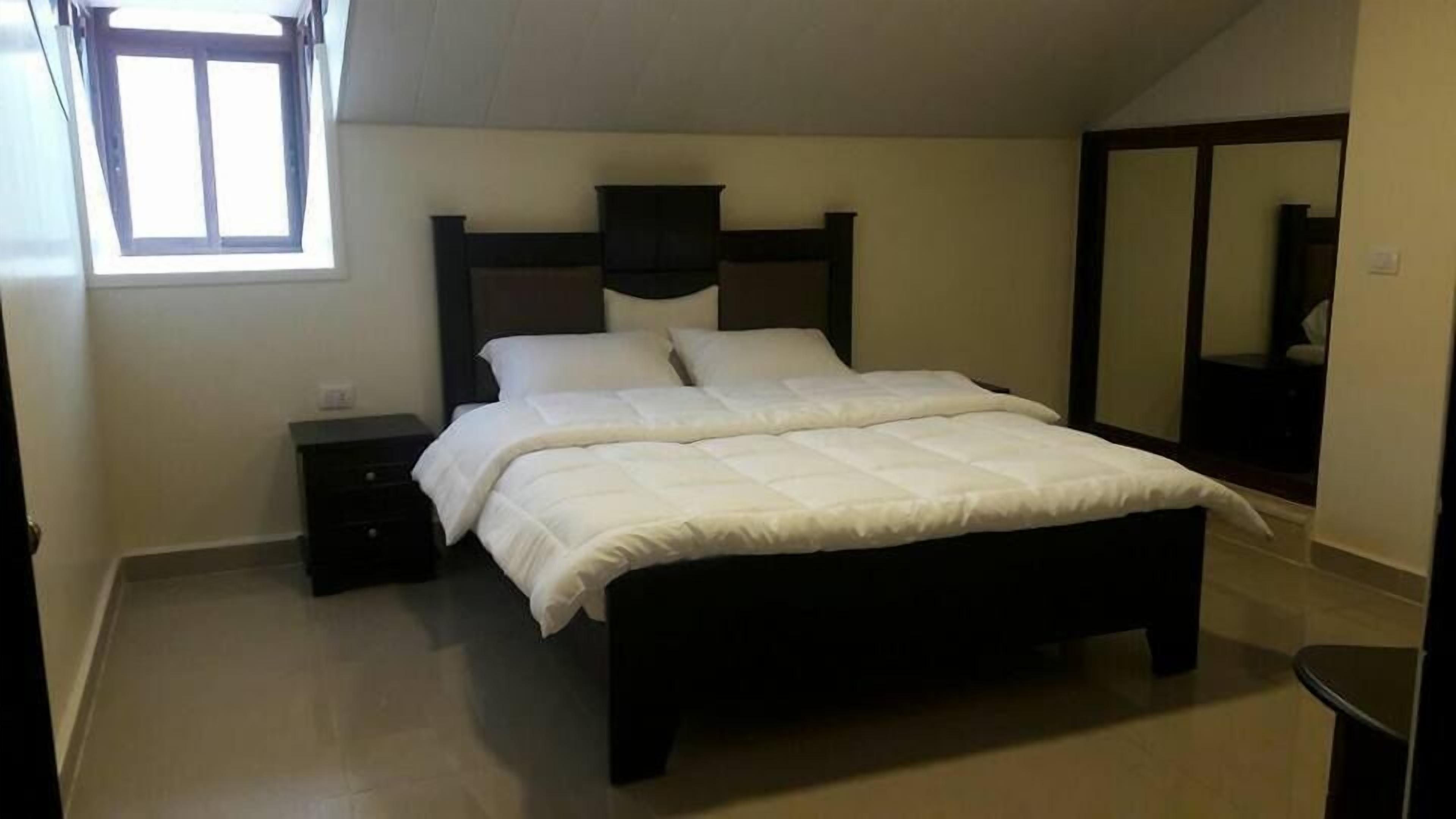 A bedroom with a bed, a nightstand, a window, and a mirror.