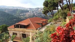 A hillside building with a red-tiled roof and stone walls, surrounded by greenery and trees. - Pinewood Hotel (Jeita)