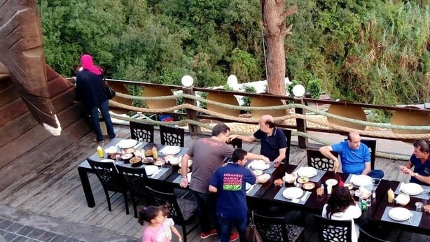 An outdoor dining area with tables and chairs, surrounded by greenery and a wooden deck. - Pinewood Hotel (Jeita)
