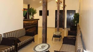 A lobby with a sofa, chairs, a reception desk, and a decorative plant. - Pinewood Hotel (Jeita)