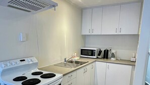 A compact kitchen with white cabinets, a stove, microwave, and a sink.