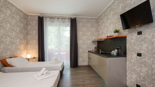 Habitación de hotel con dos camas, kitchenette, televisión montada en la pared y ventana con cortinas.