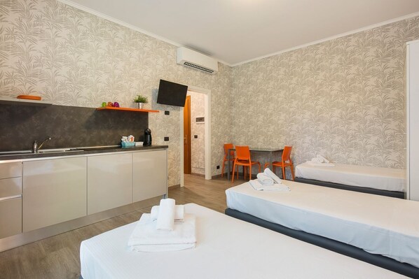 A hotel room with a kitchenette, two beds, a TV, and a small dining area.