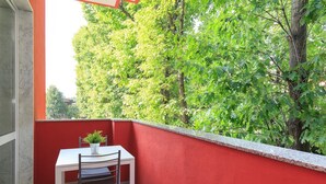 Un balcón con una pared roja, una mesa blanca y una planta en maceta.