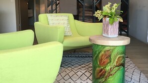 Un salon moderne avec un canapé vert, une table basse ronde agrémentée d’un arrangement floral, et une grande fresque abstraite sur le mur.
