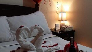 Une chambre d’hôtel avec un lit, un bouquet de roses rouges, une bouteille de vin et un panier.