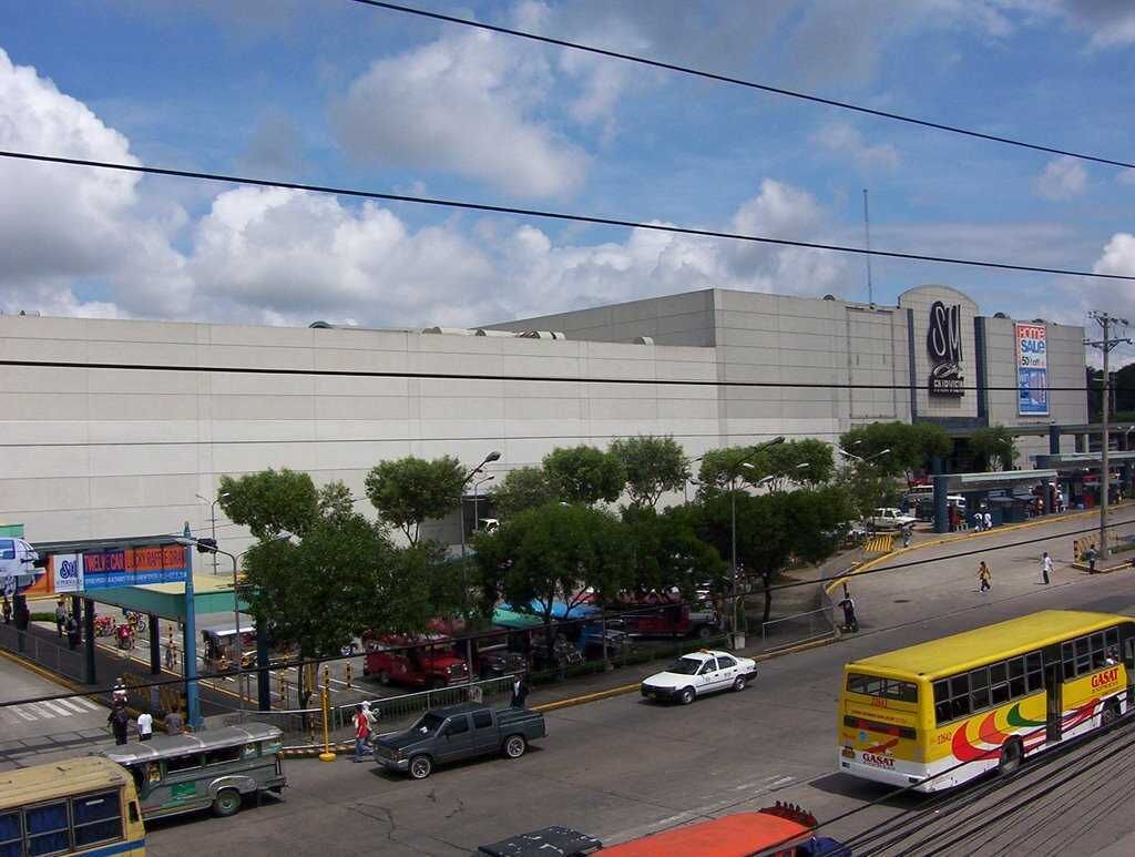 Un edificio grande con un letrero llamativo, un autobús amarillo y algunos coches en la calle.