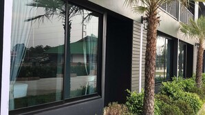 A modern building with large windows, a balcony, and well-maintained landscaping including palm trees and shrubs. - Nitta Ville (Hang Chat)
