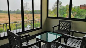A balcony with a glass table and four wooden chairs, overlooking a rural landscape with fields and trees. - Nitta Ville (Hang Chat)