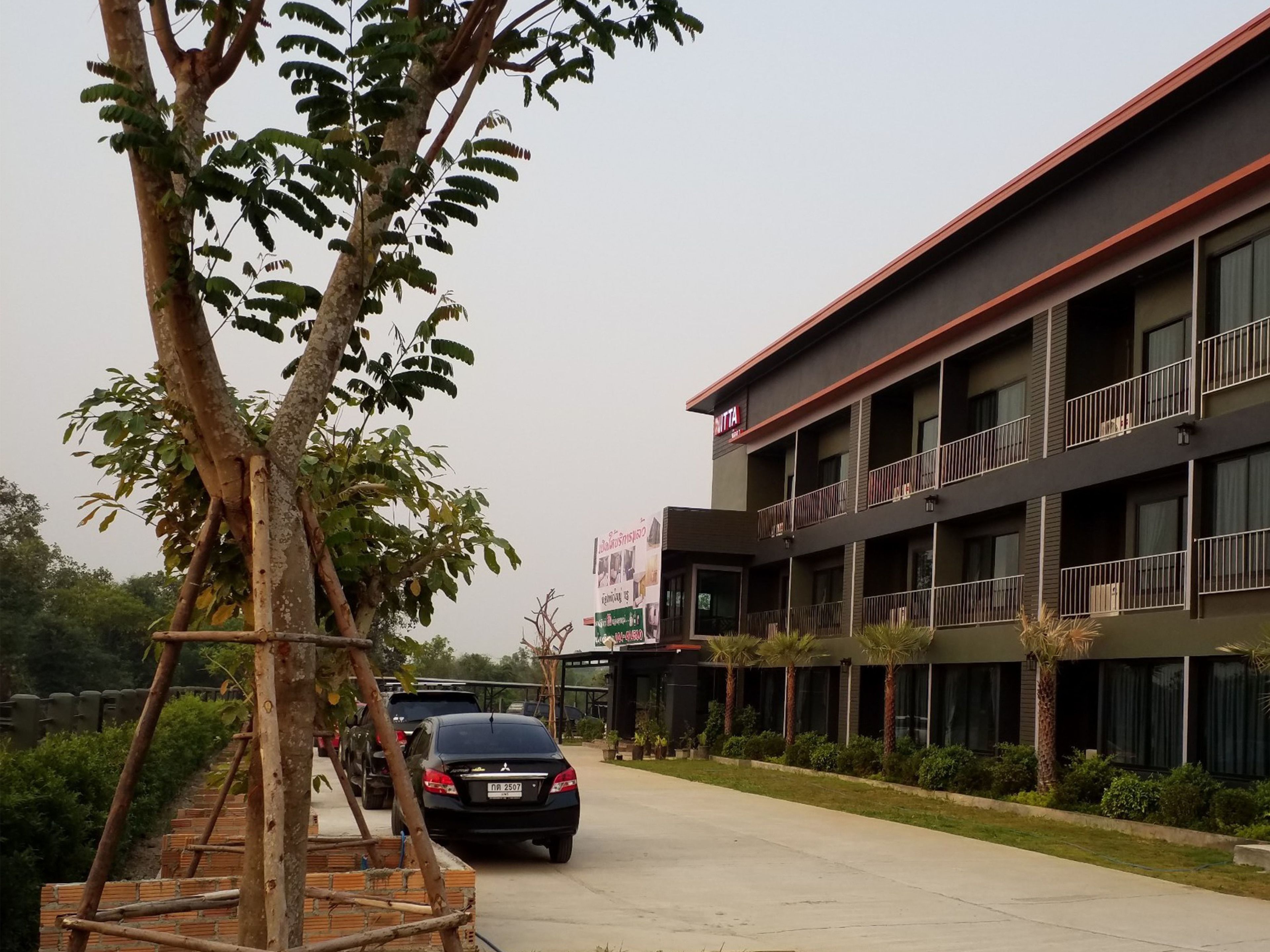 Un edificio de varios pisos con balcones, un estacionamiento y un árbol en primer plano.