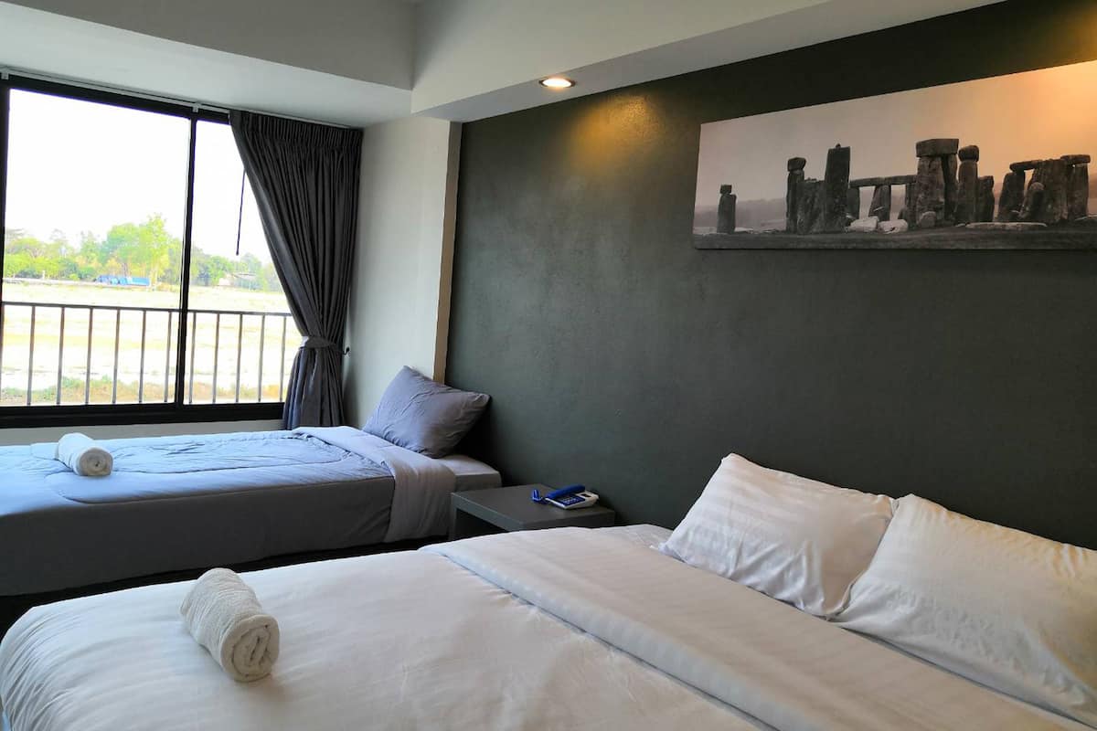 A hotel room with two beds, a painting of Stonehenge, a window with curtains, and a view of a parking area.