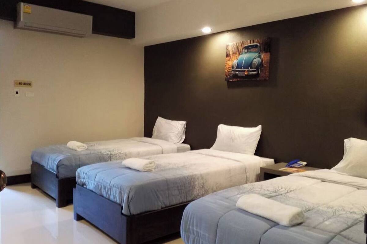A hotel room with three single beds, a dark headboard, a wall-mounted air conditioner, and a framed picture above the beds.