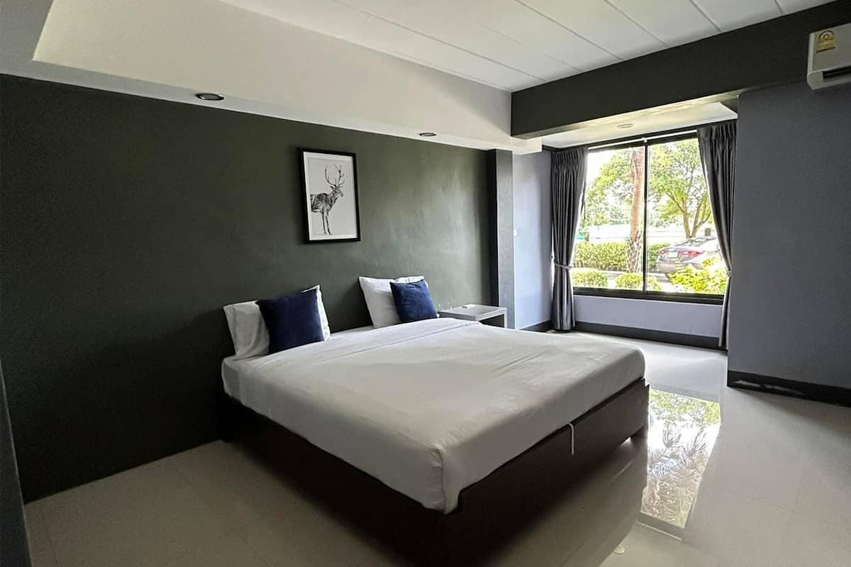 A modern bedroom with a large bed, a nightstand, a framed picture on the wall, and a window with curtains.