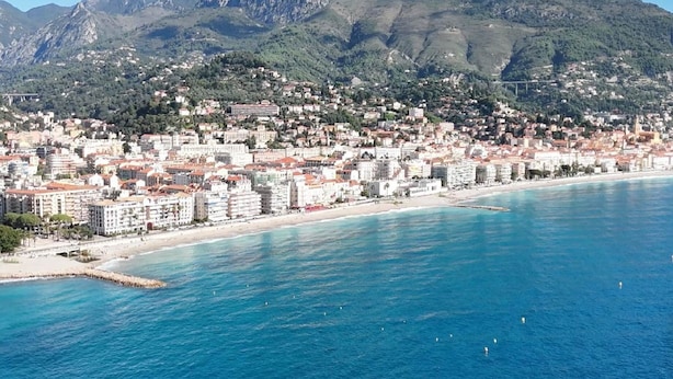 Un paisaje costero con playa y montañas al fondo.