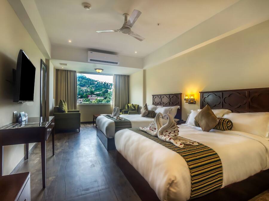 A hotel room with a large bed, a desk, a television, and a view of a mountainous landscape.