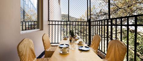 A dining table set for six with chairs, a window, and a view of trees and buildings.