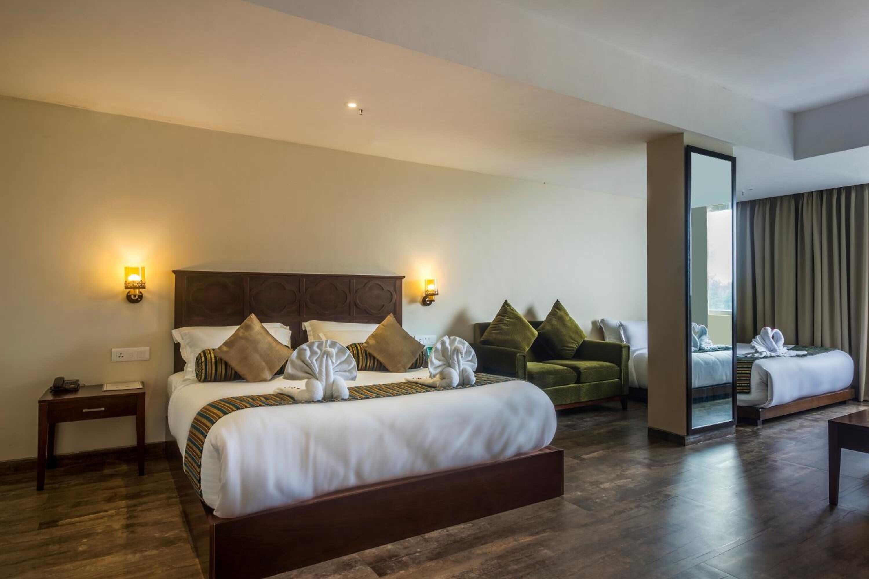 A hotel room with a large bed, a sofa, a desk, and a mirror.