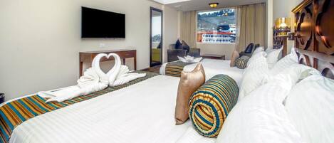 Quarto de hotel com uma cama grande, uma TV fixada na parede e vista para um edifício pela janela.