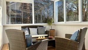 A sunroom with wicker furniture, a bench, and a potted plant. - Large penthouse by the sea - box seat on the fjord - (Glücksburg (Ostsee))