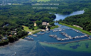 An aerial view of a marina with boats docked, surrounded by lush greenery and a river.