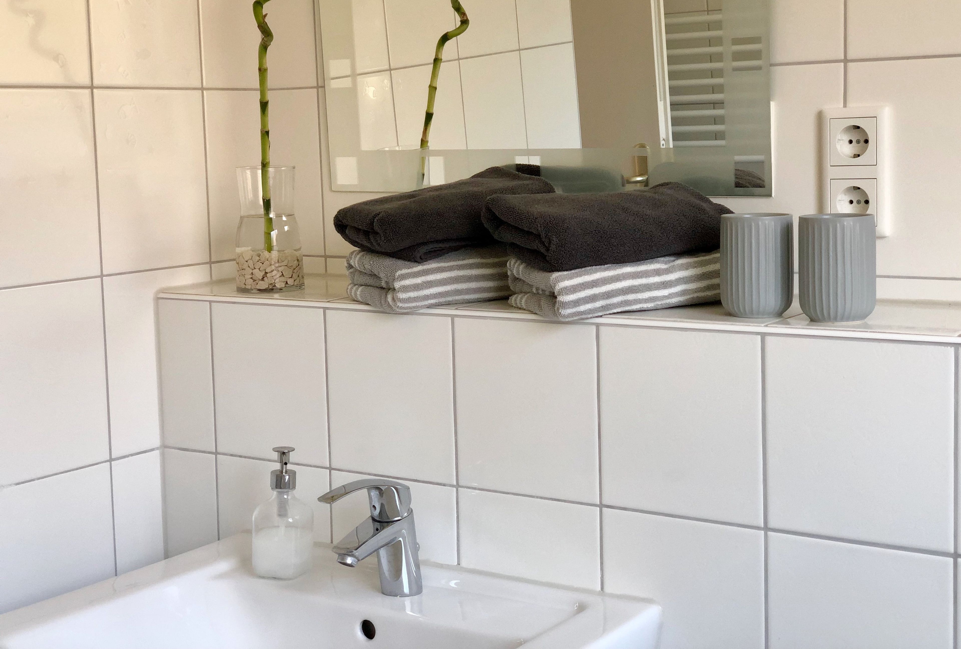 Een badkamer met witte tegels, een wastafel, een spiegel en twee bamboe planten.