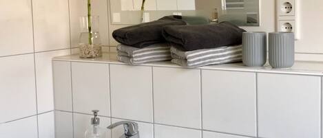 Een badkamer met witte tegels, een wastafel, een spiegel en twee bamboe planten.