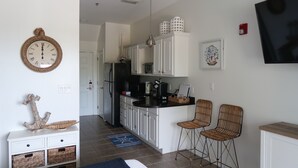 Une cuisine moderne avec des meubles blancs, un plan de travail noir et deux tabourets de bar en osier.
