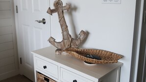 Une console blanche avec un panier tressé et un élément décoratif en forme d’ancre en bois.