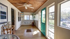 Una habitación con techo de madera, ventilador de techo, ventanas amplias, una puerta verde, un banco y una planta.